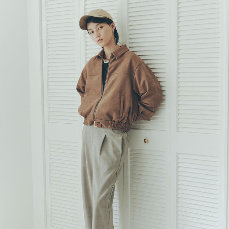 コムサイズム　黒いシャツに茶色のブルゾンを羽織り、グレーのズボンを履いた女性の写真