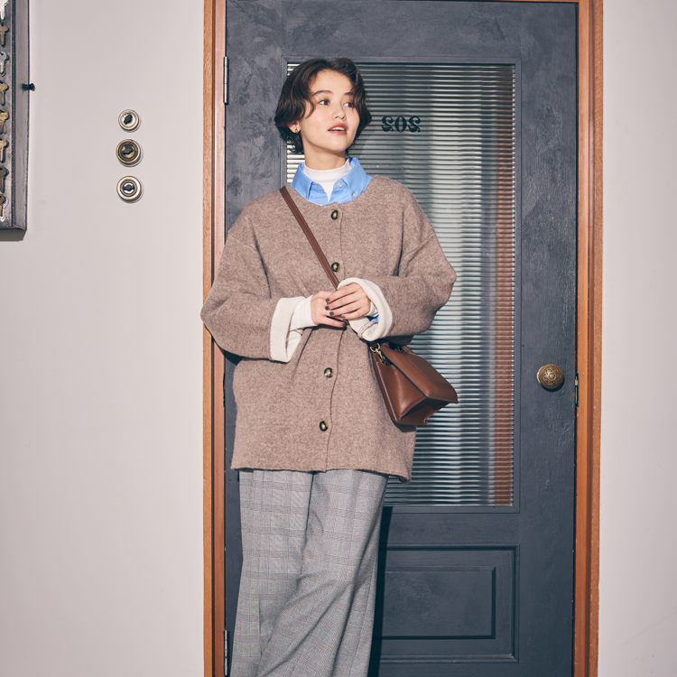 コムサイズム　白いカットソーに水色のシャツ、茶色のコーディガンを羽織り、グレーのズボンを履いた女性の写真