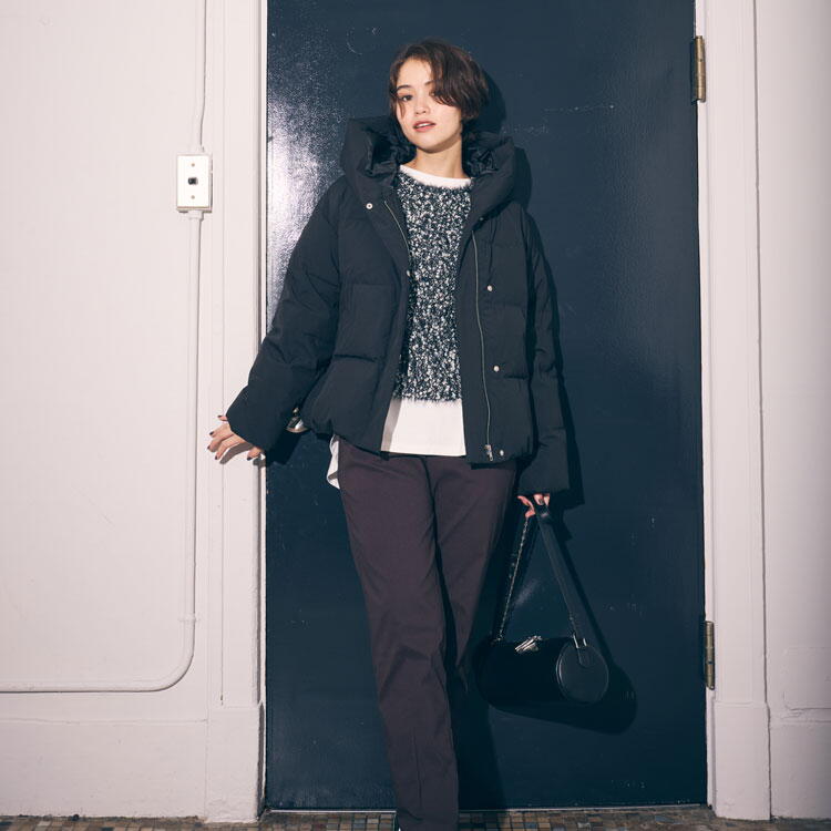 コムサイズム　白いカットソーにグレーのニット、黒いダウンを羽織り、茶色いズボンを履いた女性の写真