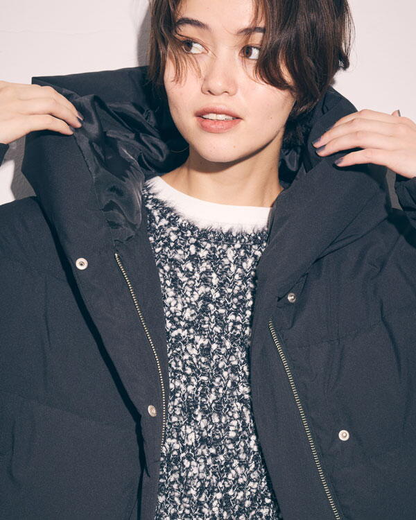 コムサイズム　白いカットソーにグレーのニット、黒いダウンを羽織り、茶色いズボンを履いた女性の写真